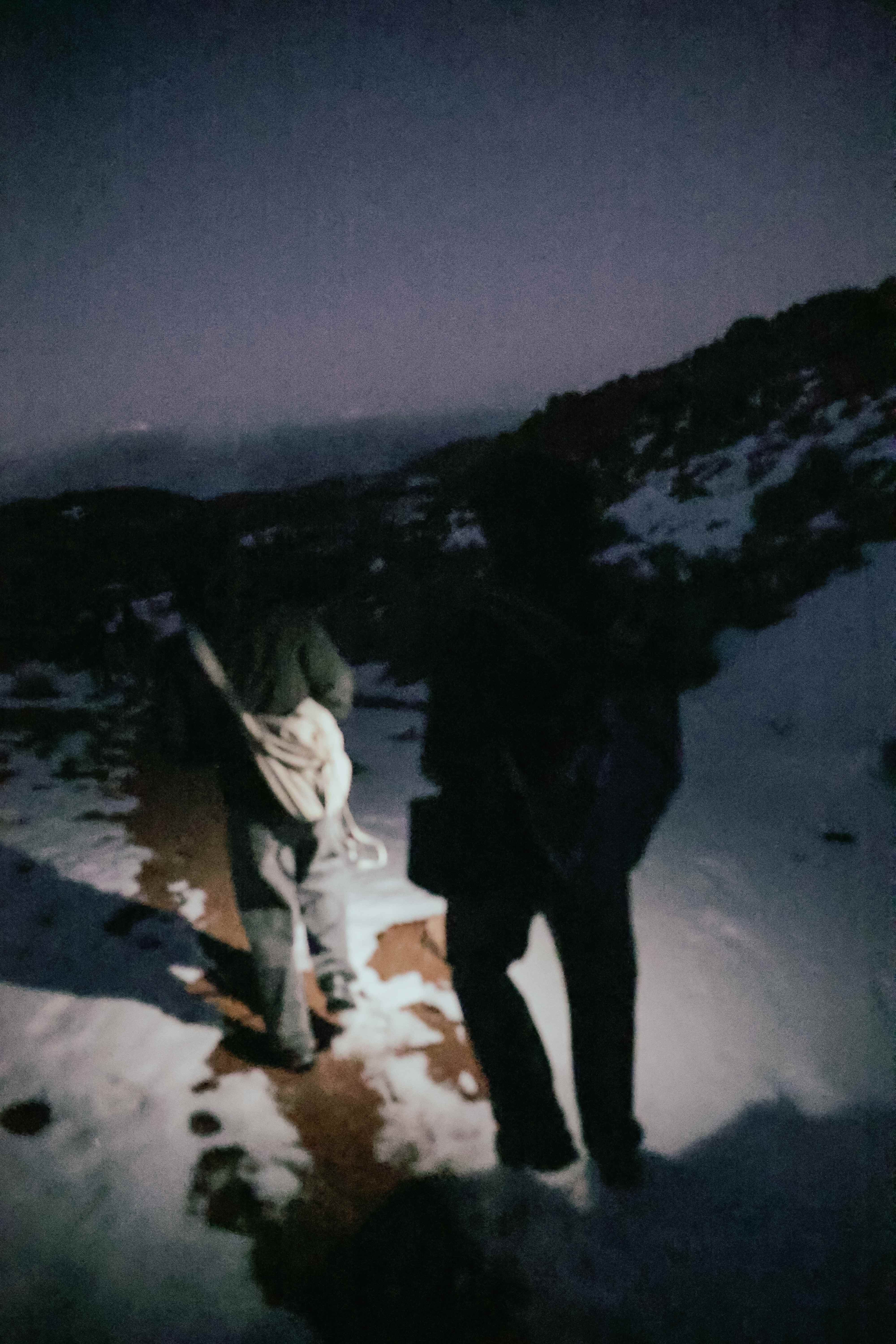 Two silhouetted figures hiking a snowy trail at dusk with a lantern
