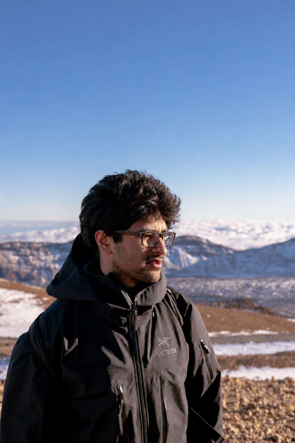 Portrait on a snowy mountain ridge with Arc'teryx jacket and snow-capped peaks behind