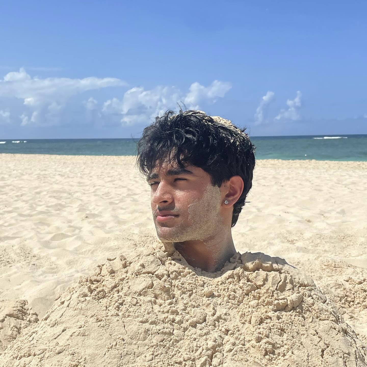 Anand buried in beach sand up to his neck with the ocean behind him